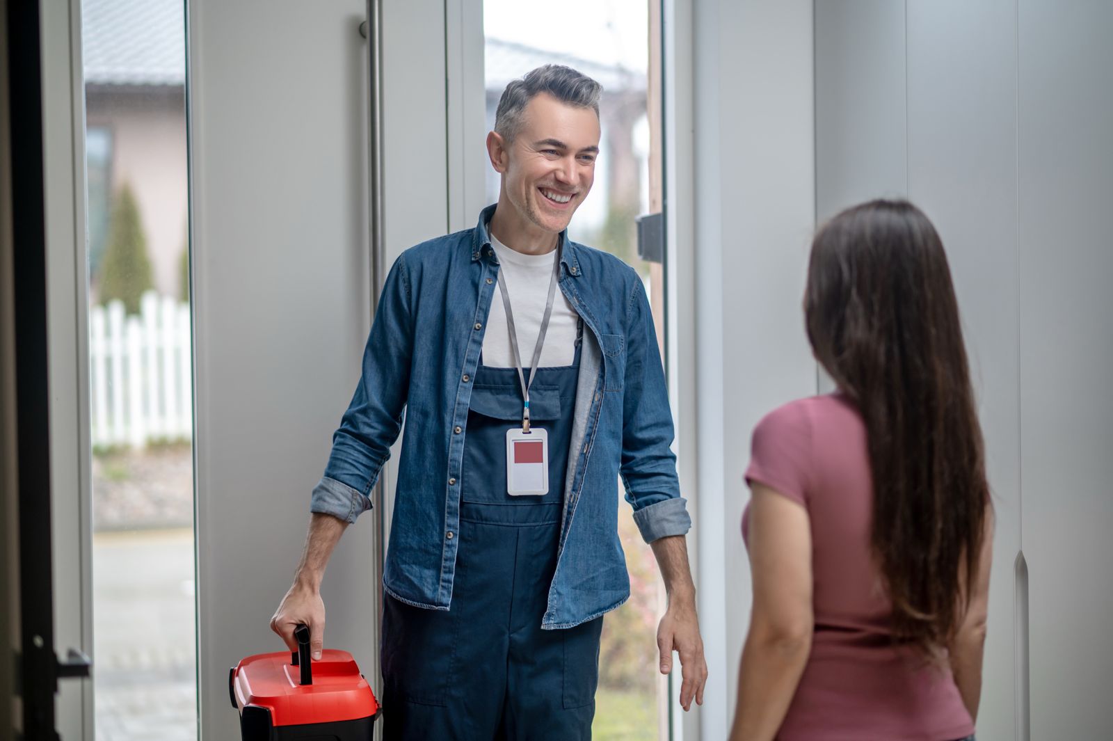 Smiling technician arriving at a customer’s home carrying a red toolbox.